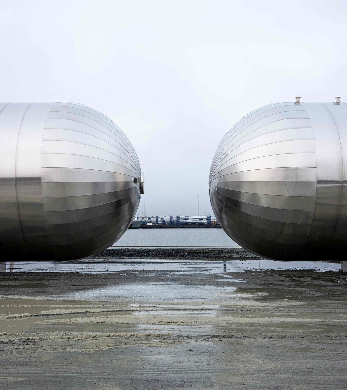 Zwei große CO2-Lagertanks aus Metall stehen an einem Hafen.