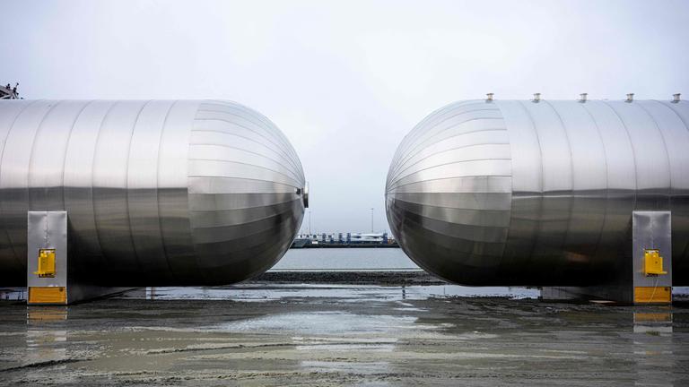 Zwei große CO2-Lagertanks aus Metall stehen an einem Hafen.