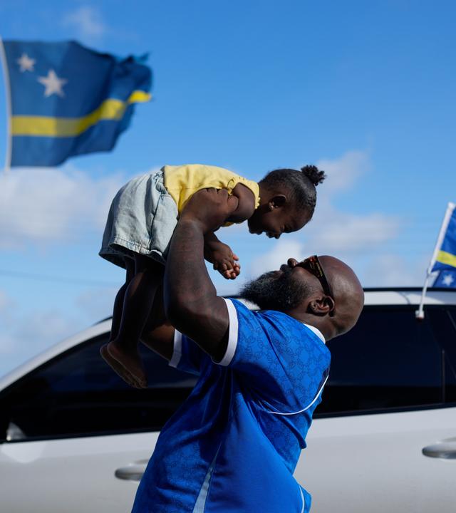 Brenton Balentien, bekannt als „Blue Face“ und Anführer der Fußballfans der Nationalmannschaft von Curaçao, hält seine Tochter in Willemstad hoch.