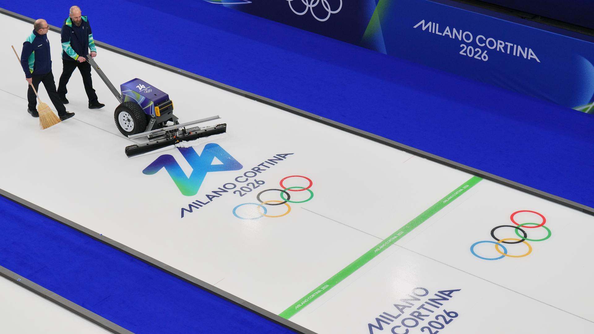 Zwei Männer präparieren die Curling-Bahn vor den Olympischen Winterspielen 2026