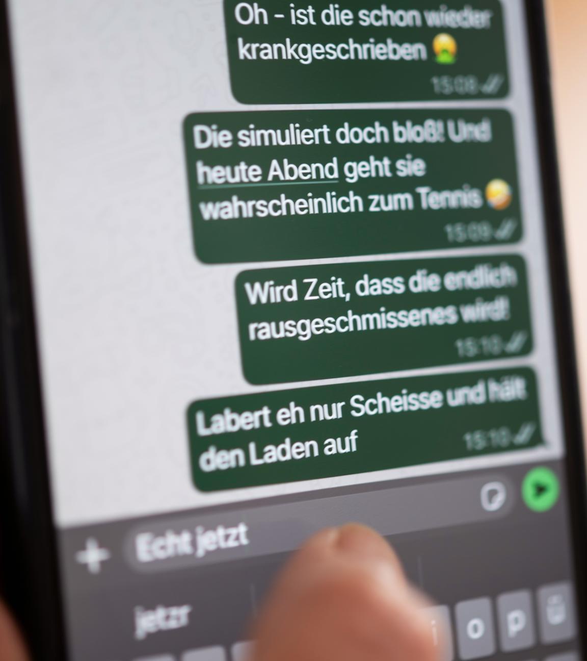 Eine Person hält ein Smartphone in der Hand, auf dessen Bildschirm beleidigende Nachrichten in einem Chat zu sehen sind (gestellte Szene).