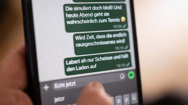 Eine Person hält ein Smartphone in der Hand, auf dessen Bildschirm beleidigende Nachrichten in einem Chat zu sehen sind (gestellte Szene).