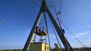Techniker reparieren eine Oberleitung eines Oberleitungsbusses neben den Schäden (R) an einem Brückenpfeiler nach einem Drohnenangriff auf die Nordbrücke in Kiew am 3. Oktober 2026 im Zuge der russischen Invasion in der Ukraine