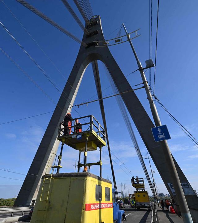 Techniker reparieren eine Oberleitung eines Oberleitungsbusses neben den Schäden (R) an einem Brückenpfeiler nach einem Drohnenangriff auf die Nordbrücke in Kiew am 3. Oktober 2026 im Zuge der russischen Invasion in der Ukraine