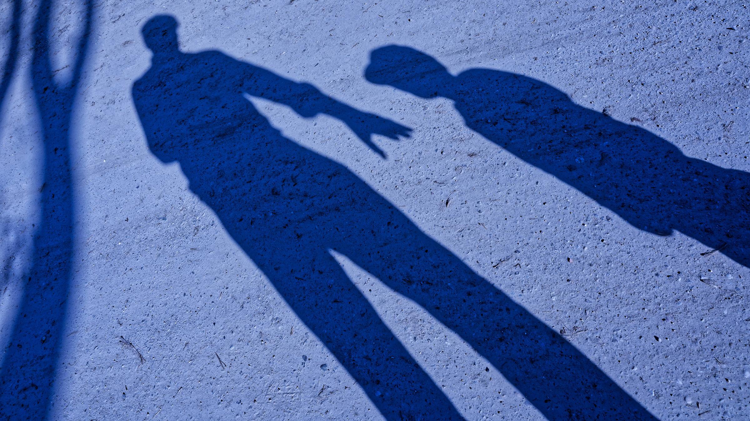 Der Schatten von einem Mann, der die Hand nach einem Kind ausstreckt in der Dämmerung.