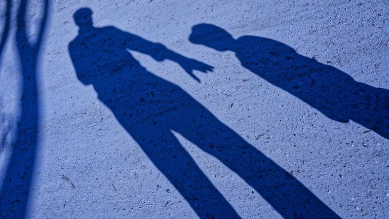 Der Schatten von einem Mann, der die Hand nach einem Kind ausstreckt in der Dämmerung.