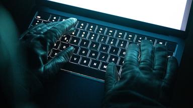 Eine Person tippt mit behandschuhten Händen auf einer beleuchteten Laptop-Tastatur.