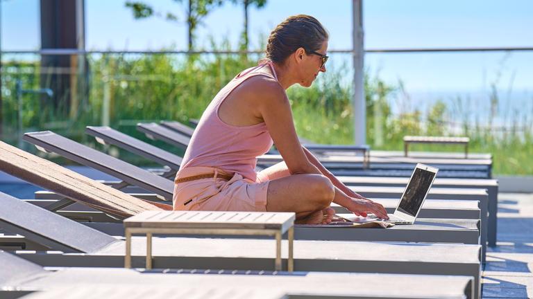 Frau mit Laptop auf Liegestuhl