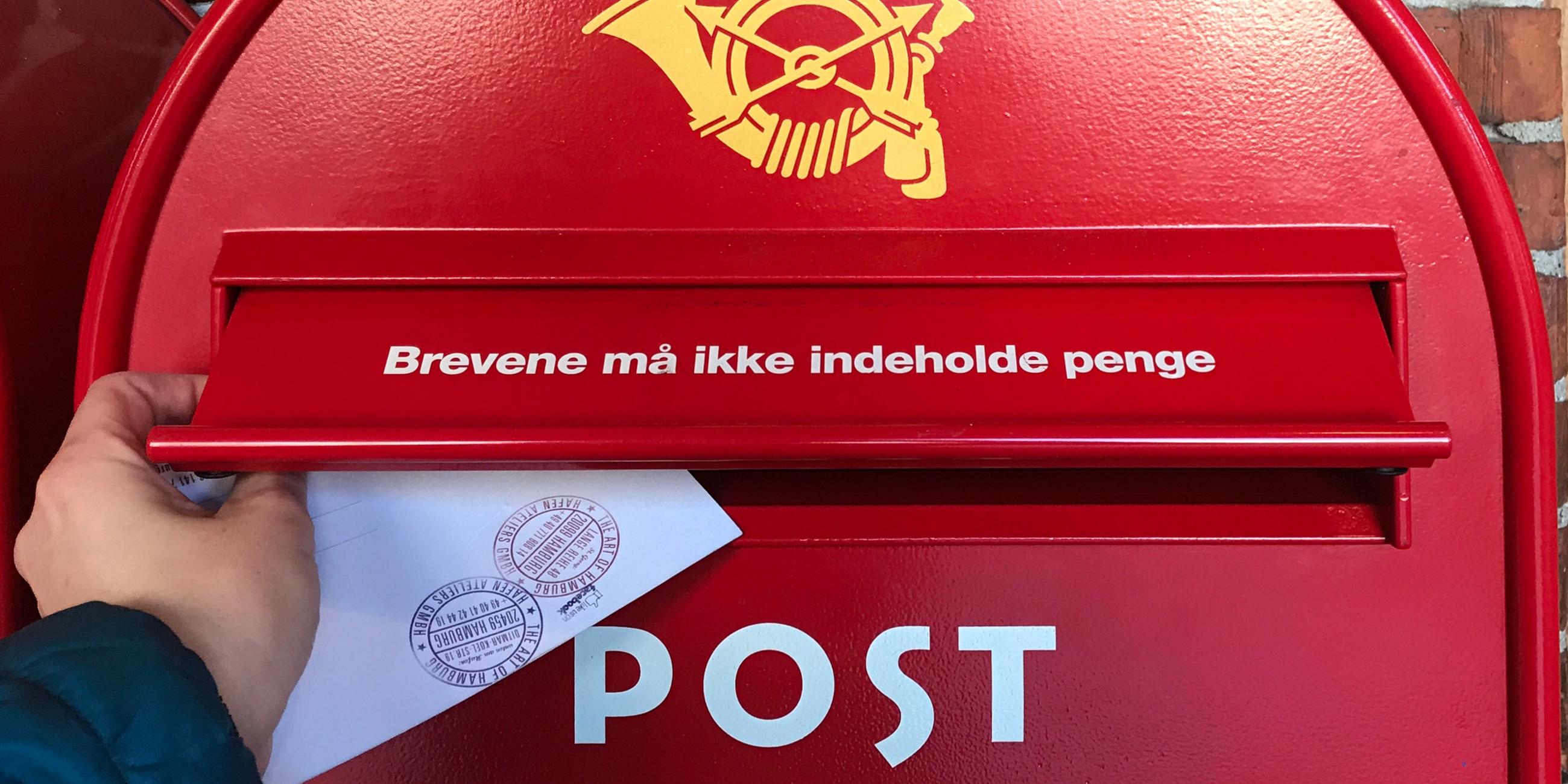 Ein dänischer Briefkasten in einem Dunkelrot. Es wird gerade ein Brief reingeschmissen