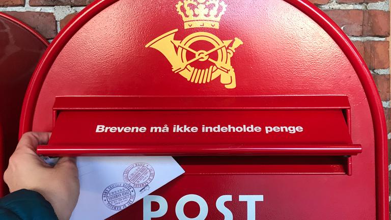 Ein dänischer Briefkasten in einem Dunkelrot. Es wird gerade ein Brief reingeschmissen