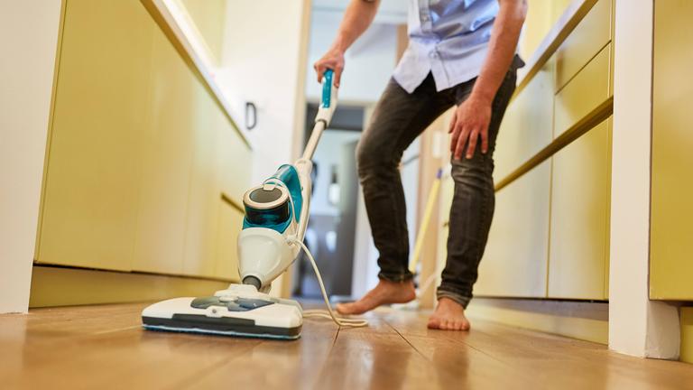 Ein putzt den Flur mit einem Dampfreiniger.