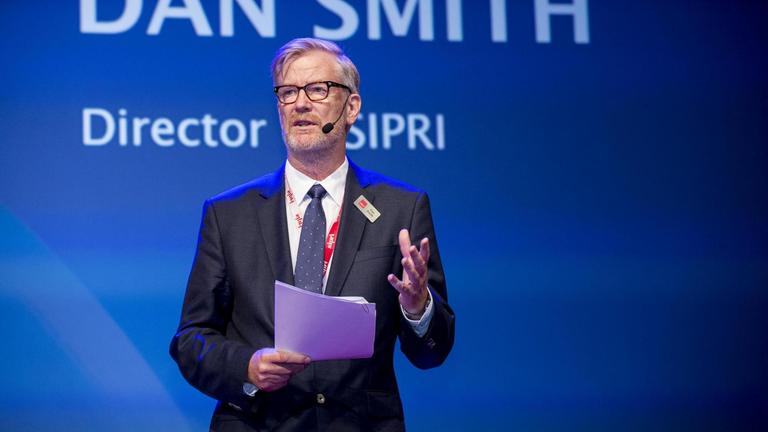 Dan Smith, der Direktor von SIPRI, steht vor einem blauen Hintergund und hält eine Rede.