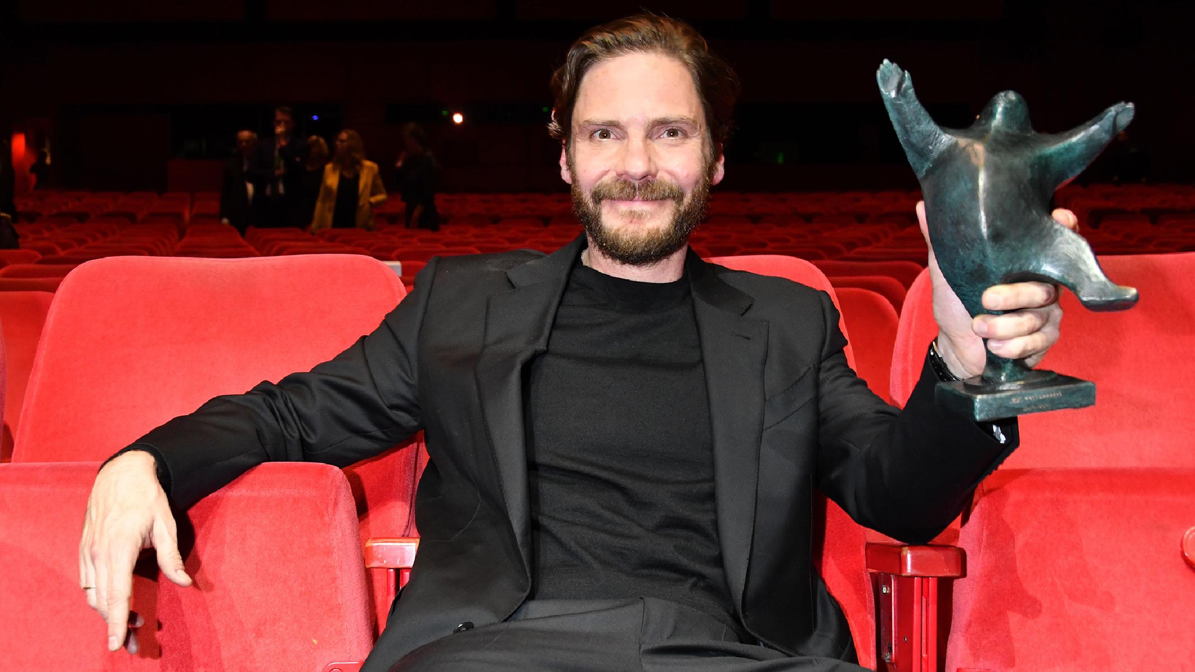 Daniel Brühl sitzt im Theater am Potsdamer Platz. In der rechten Hand hält er den "B.Z."-Kulturpreis.