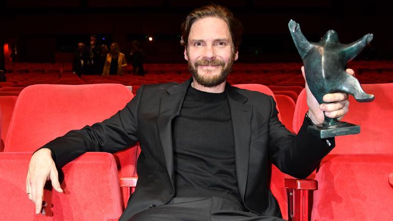 Daniel Brühl sitzt im Theater am Potsdamer Platz. In der rechten Hand hält er den "B.Z."-Kulturpreis.