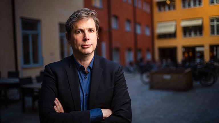 Porträtfoto eines Mannes mit leicht graumeliertem Haar, der einen Anzug mit blauem Hemd trägt.