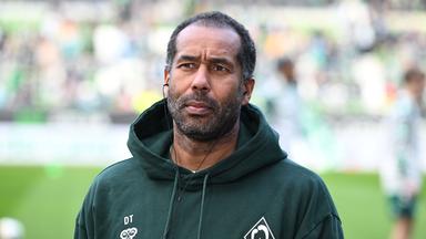Daniel Thioune steht auf einem Fußballfeld.