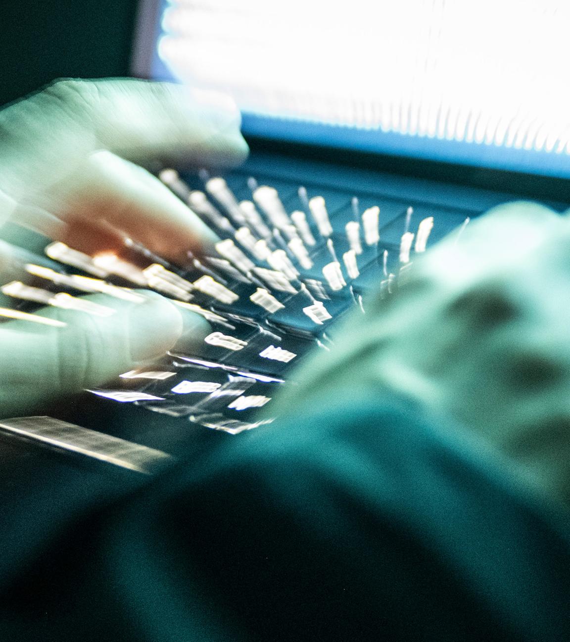 Eine Person tippt mit den Fingern auf einer beleuchteten Laptop-Tastatur. (Gestellte Szene, Aufnahme mit Langzeitbelichtung)