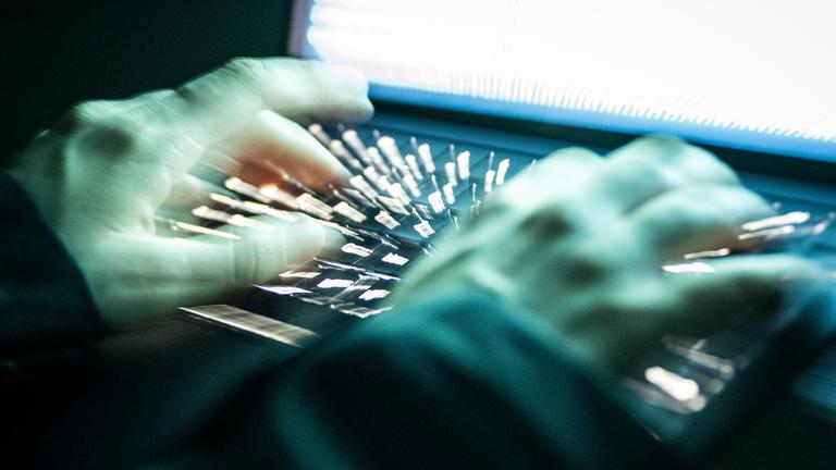 Eine Person tippt mit den Fingern auf einer beleuchteten Laptop-Tastatur. (Gestellte Szene, Aufnahme mit Langzeitbelichtung)