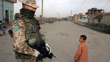  Ein Bundeswehrsoldat der Internationalen Afghanistan- Schutztruppe (ISAF) mit kugelsicherer Weste beobachtet am Montag, dem 04.08.2003 einen an ihm vorbei gehenden afghanischen Jungen in Karteparwan, einem nordoestlichen Stadtteil von Kabul.  