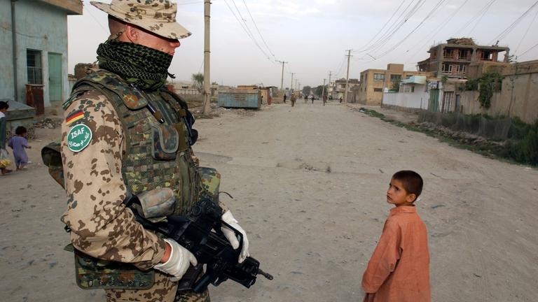  Ein Bundeswehrsoldat der Internationalen Afghanistan- Schutztruppe (ISAF) mit kugelsicherer Weste beobachtet am Montag, dem 04.08.2003 einen an ihm vorbei gehenden afghanischen Jungen in Karteparwan, einem nordoestlichen Stadtteil von Kabul.  