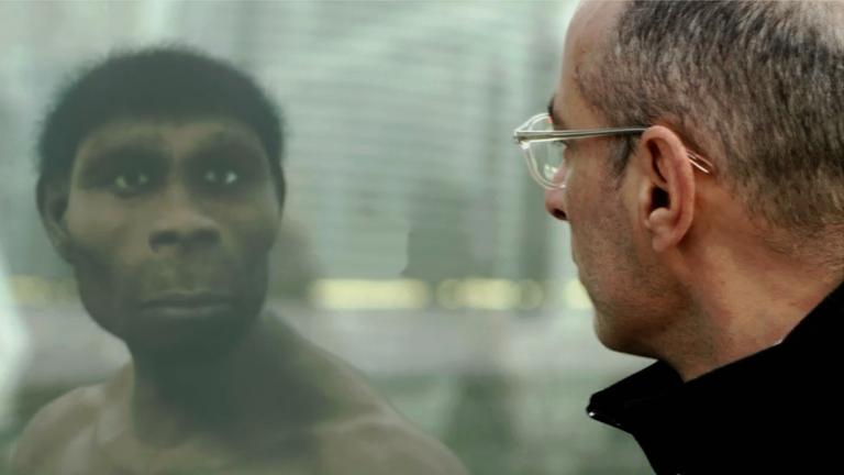 Ein Mann sieht in seinem Spiegelbild einen frühen Homo sapiens.