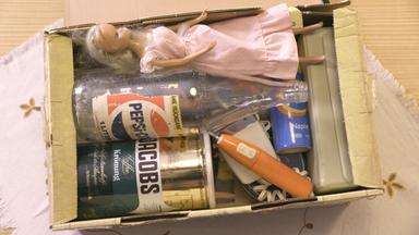 "Das war dann mal weg: Westpaket, Intershop & Kaderakte": Blick in ein geöffnetes, altes Westpaket. Zu sehen sind unter anderem eine Kaffeedose, eine leere Cola-Flasche und eine Barbiepuppe.