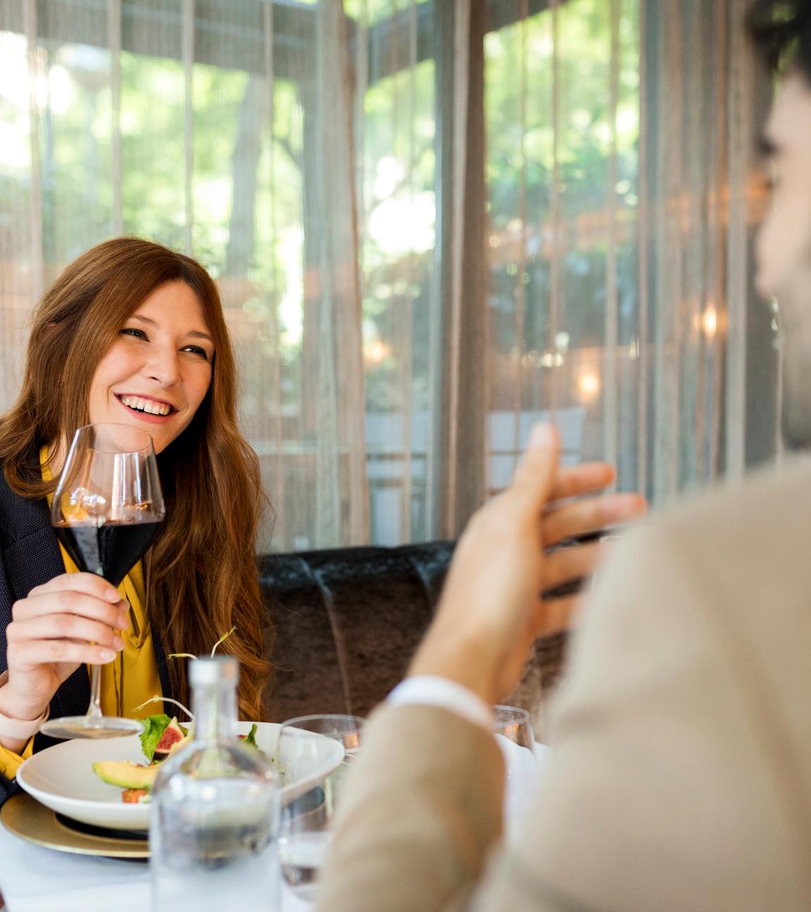 Lächelnde Frau mit einem Glas Rotwein, die einen Mann in einem Restaurant ansieht.