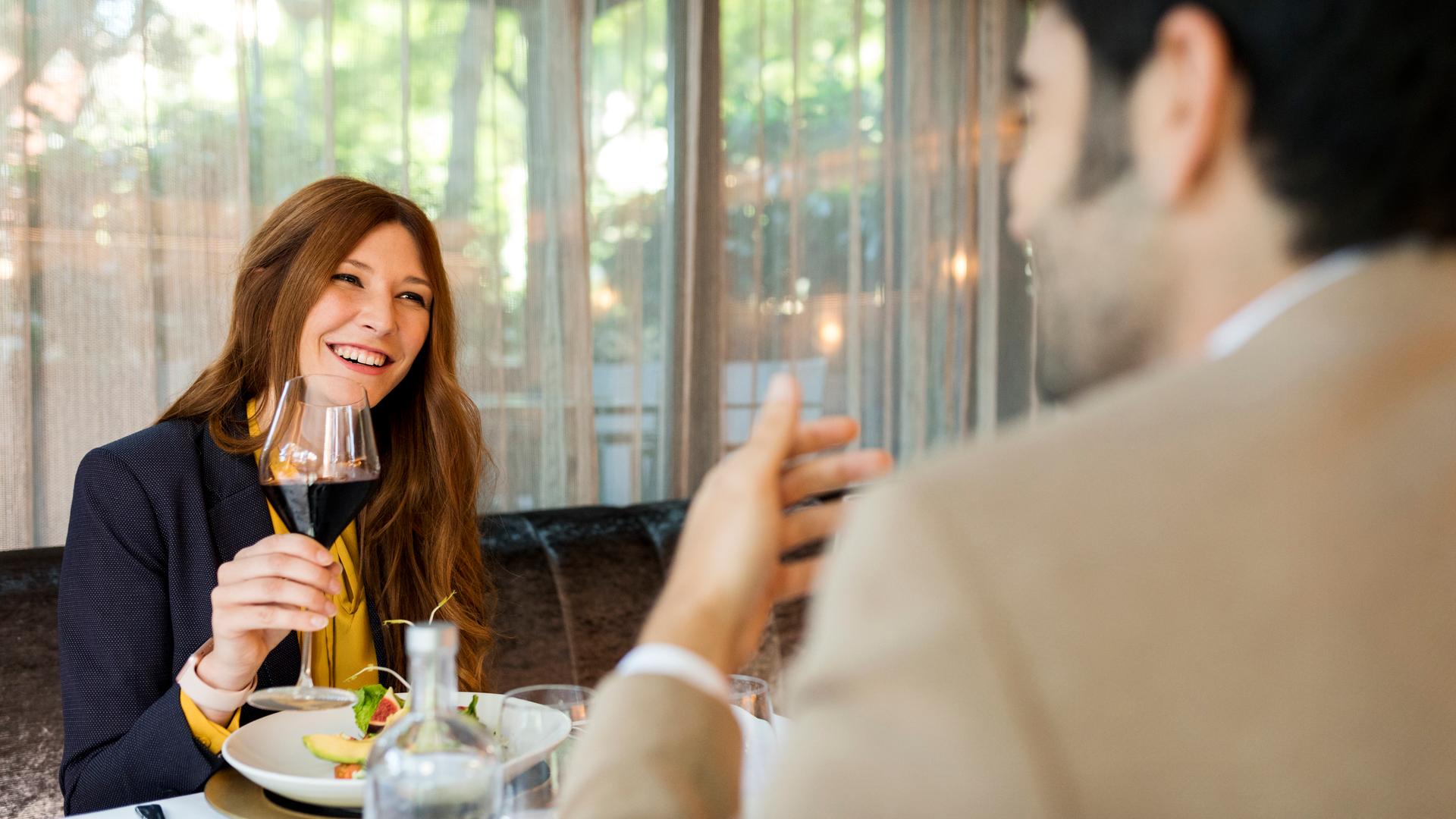 Lächelnde Frau mit einem Glas Rotwein, die einen Mann in einem Restaurant ansieht.