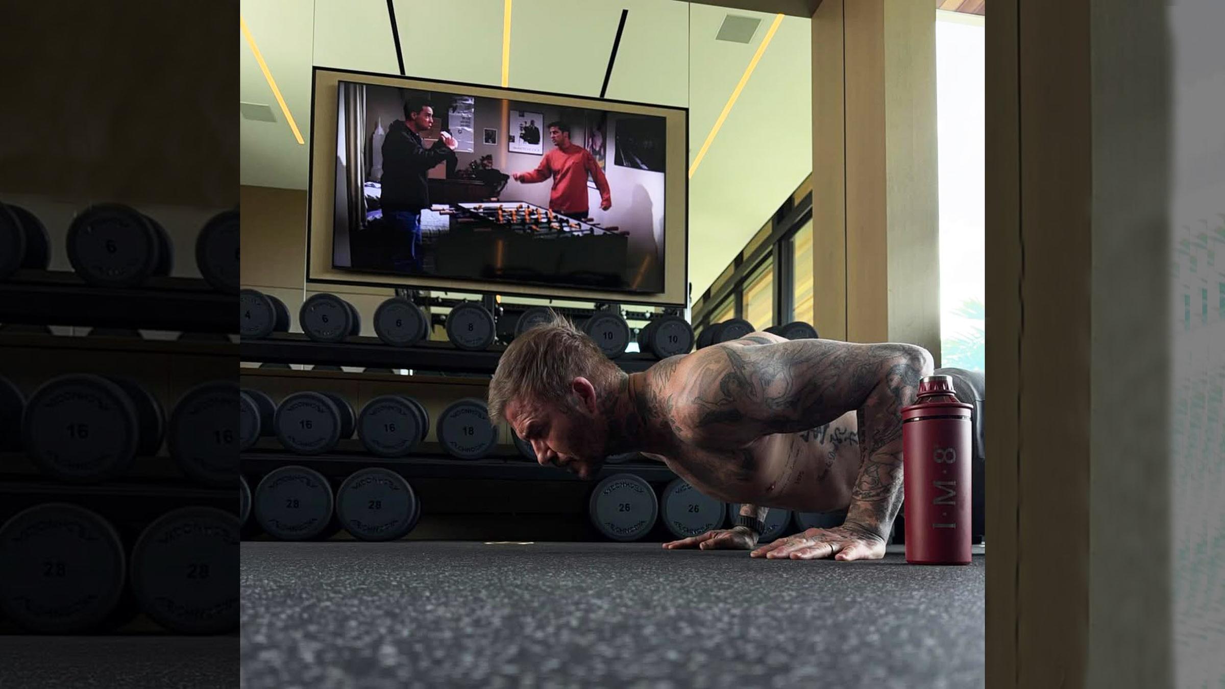 David Beckham macht Liegestütze, während im Hintergrund auf einem Fernseher die Serie "Friends" läuft.