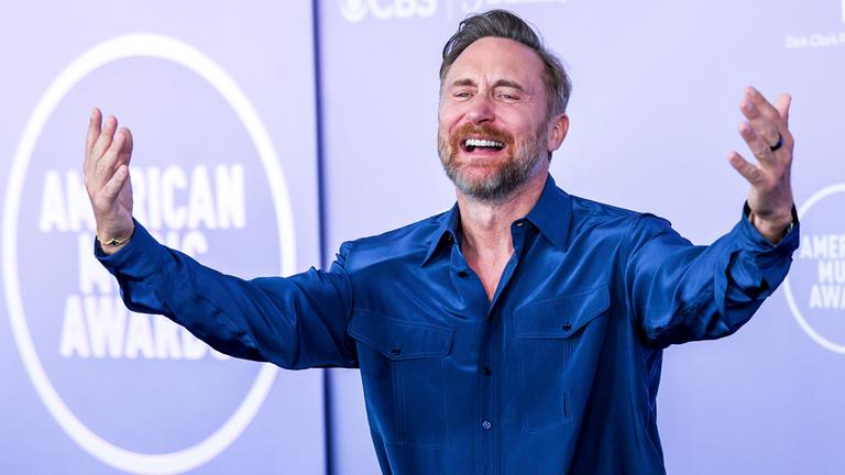 David Guetta steht mit erhobenen Armen auf einer Bühne.