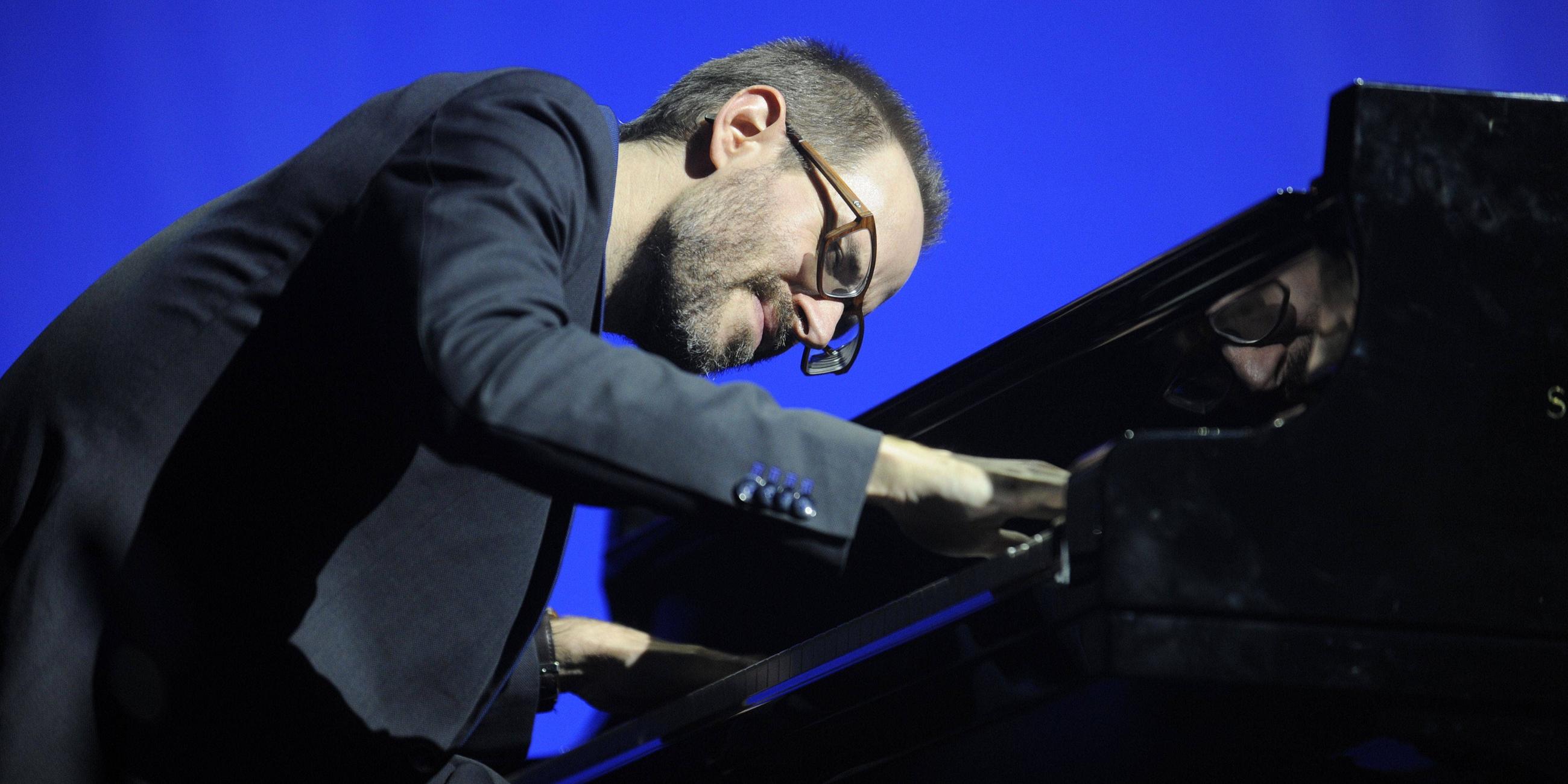Ein Mann mit Brille und Bart beugt sich über ein Klavier und spielt.