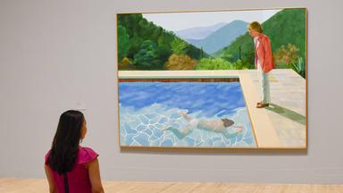 Eine Mitarbeiterin sieht sich das Gemälde „Portrait of an Artist (Pool with Two Figures)“ bei der Vorbesichtigung der Retrospektive über das Werk von David Hockney in der Tate Britain, in London, im Jahre 2017.