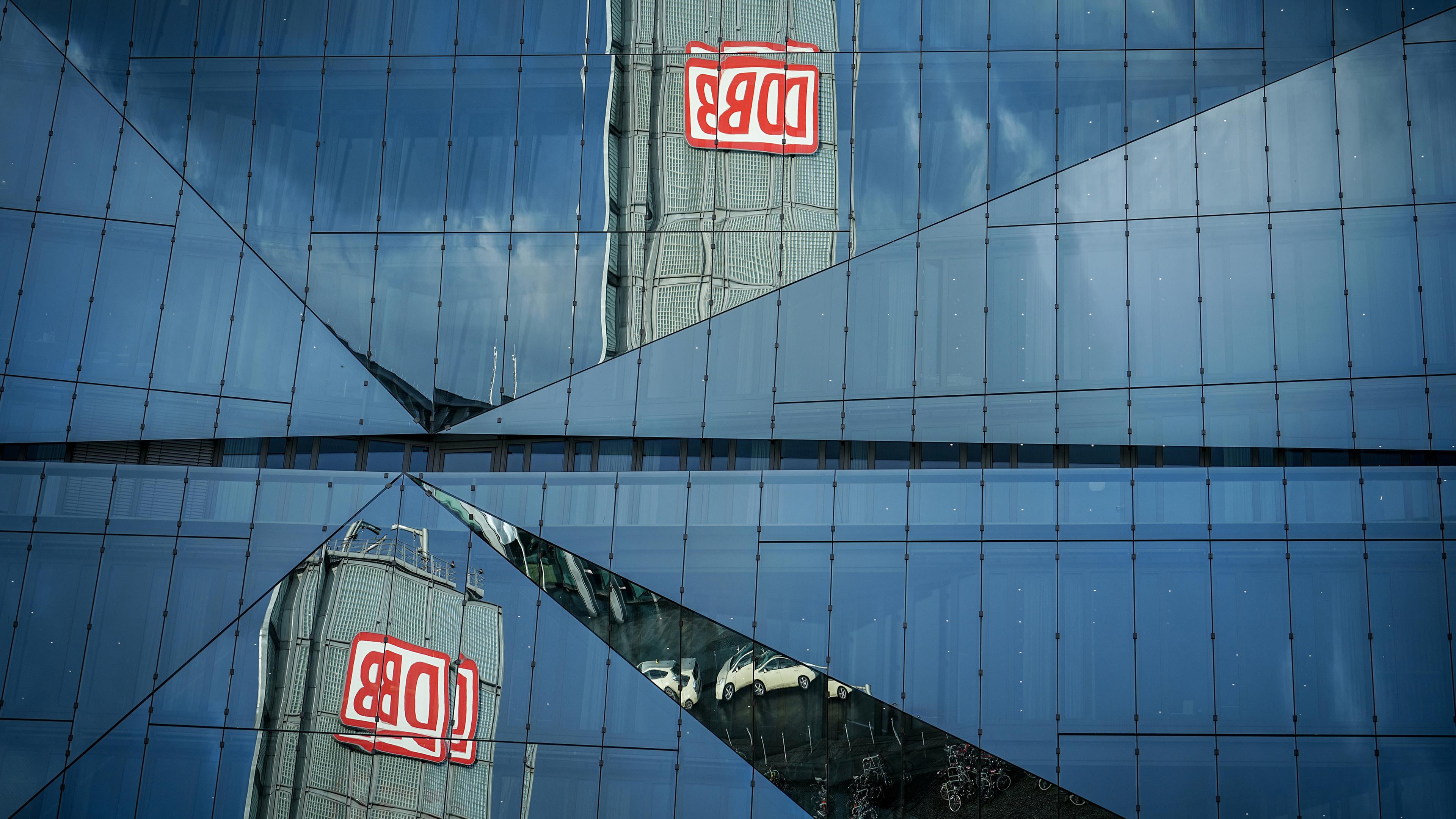 Das Logo der Bahn "DB" spiegelt sich unter bewölkten Himmel in einem Bürogebäude am Berliner Hauptbahnhof
