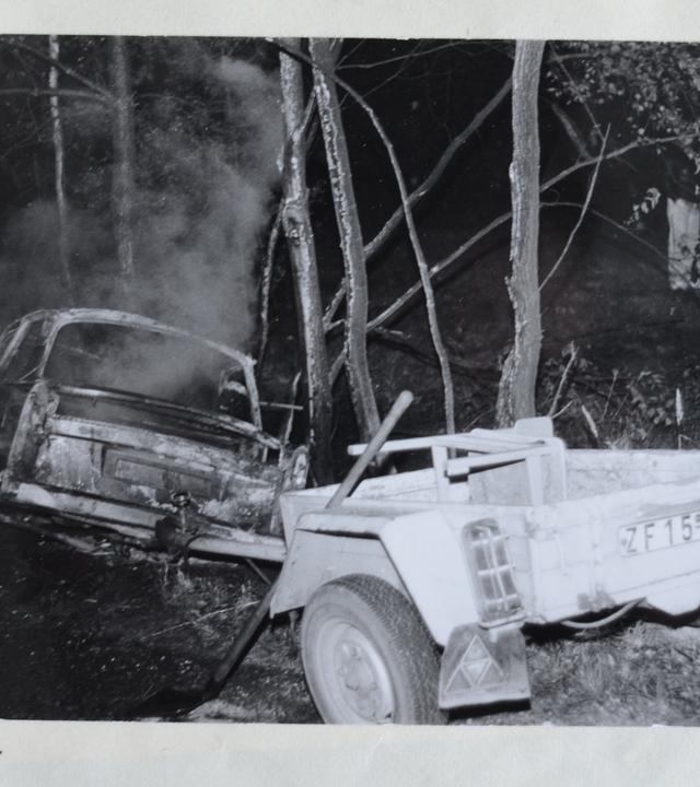 Ein abgebrannter Trabi mit Anhänger liegt nach einem Unfall in einem Wald.