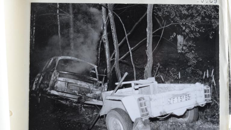 Ein abgebrannter Trabi mit Anhänger liegt nach einem Unfall in einem Wald.