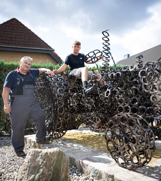 Gerhard Kähne (l) und sein Enkel Malte posieren an einem nachgebauten Traktor aus 1.500 Hufeisen.