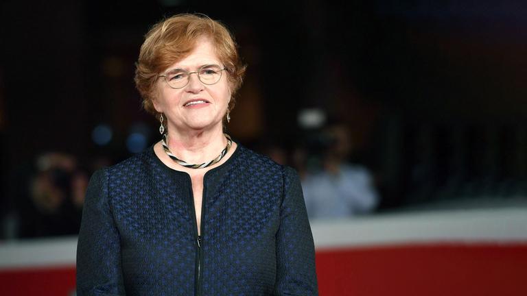 Eine Frau mit Brille und blauer Jacke und Schmuck