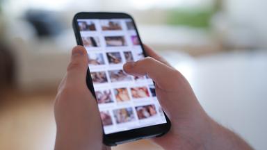Ein junger Mann schaut sich auf einem Smartphone eine Porno-Internetseite an (gestellte Szene).