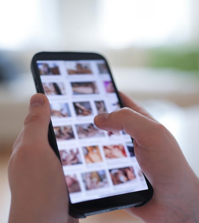 Ein junger Mann schaut sich auf einem Smartphone eine Porno-Internetseite an (gestellte Szene).