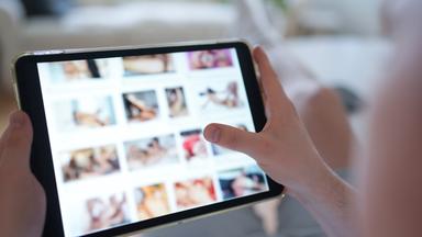 Ein junger Mann schaut sich auf einem Smartphone eine Porno-Internetseite an.