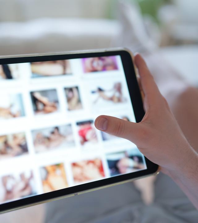 Ein junger Mann schaut sich auf einem Smartphone eine Porno-Internetseite an.