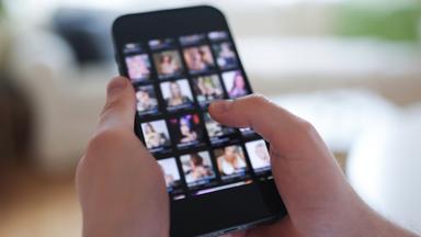 Ein junger Mann schaut sich auf einem Smartphone eine Porno-Internetseite an (gestellte Szene)