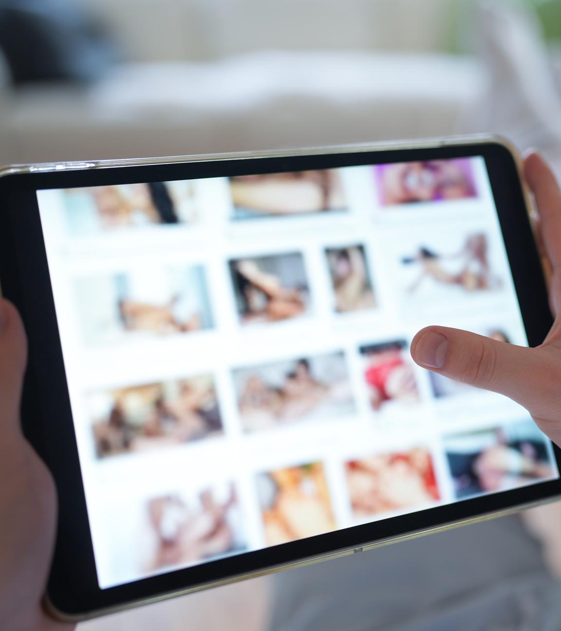 Eine Person scrollt durch das Tablet und schaut sich pornografische Inhalte an.