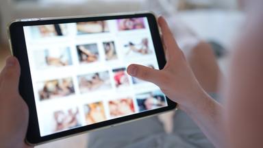 Eine Person scrollt durch das Tablet und schaut sich pornografische Inhalte an.