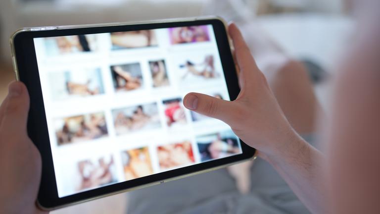 Eine Person scrollt durch das Tablet und schaut sich pornografische Inhalte an.