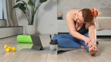 Frau übt Stretching mit Online-App zu Hause.