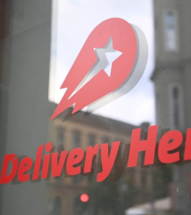 Logo und Schriftzug des Essenslieferdienstes Delivery Hero ist an einer Glasscheibe der Zentrale angebracht.