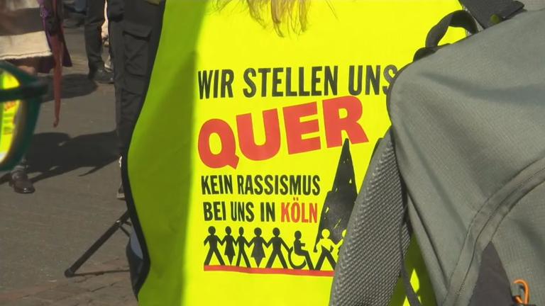 Auf dem Rücken einer gelben Warnweste steht: "Wir stellen uns Quer - kein Rassismus bei uns in Köln".
