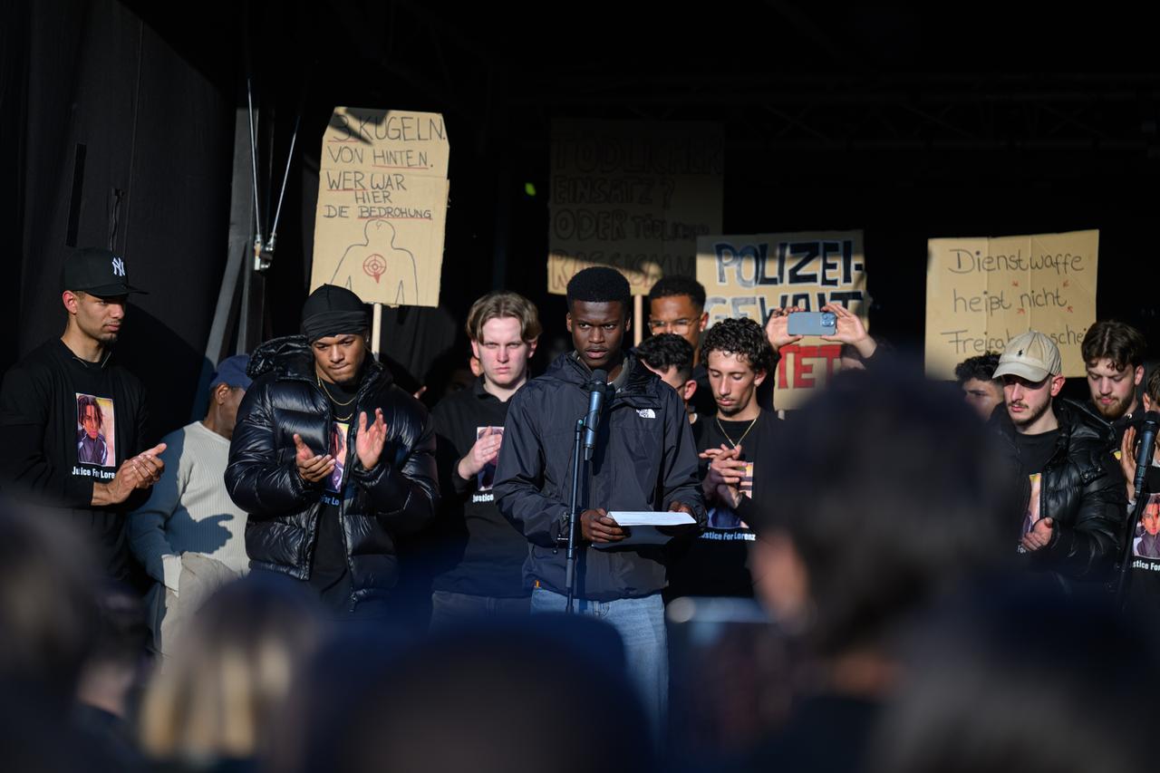 , Oldenburg: Suraj Mailitafi (Initiative Gerechtigkeit für Lorenz) spricht bei der Kundgebung nach tödlichen Polizeischüssen vor 8000-10.000 versammelten Menschen auf dem Pferdemarkt in Oldenburg. Auf der Bühne stehen Verwandte und Freunde des getöteten Lorenz. 