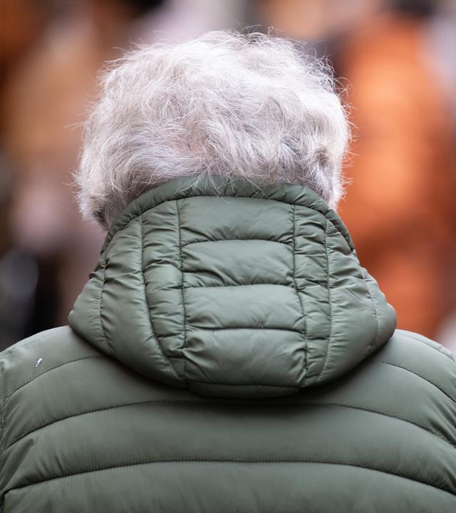 Eine ältere Frau trägt eine grüne Winterjacke. Man sieht sie nur von hinten